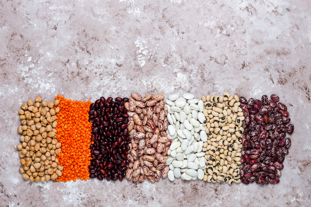 Legumes and beans assortment in different bowls on light stone background